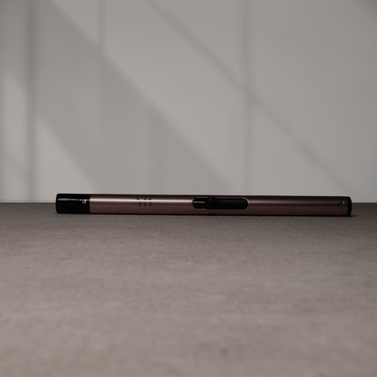 Rosé gouden aansteker met zwart mondstuk en schuifmechanisme, liggend op een grijze ondergrond met zachte schaduwen op de achtergrond.