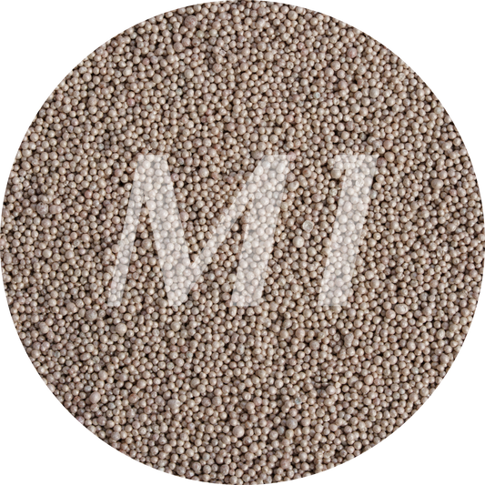Kleurstaal van bruin kaarsenzand met fijne waxparels en subtiel M1-logo op de achtergrond.