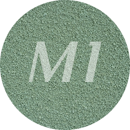 Kleurstaal van groen kaarsenzand met fijne waxparels en subtiel M1-logo op de achtergrond.
