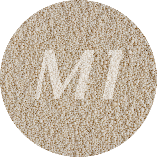 Kleurstaal van beige kaarsenzand met fijne waxparels en subtiel M1-logo op de achtergrond.