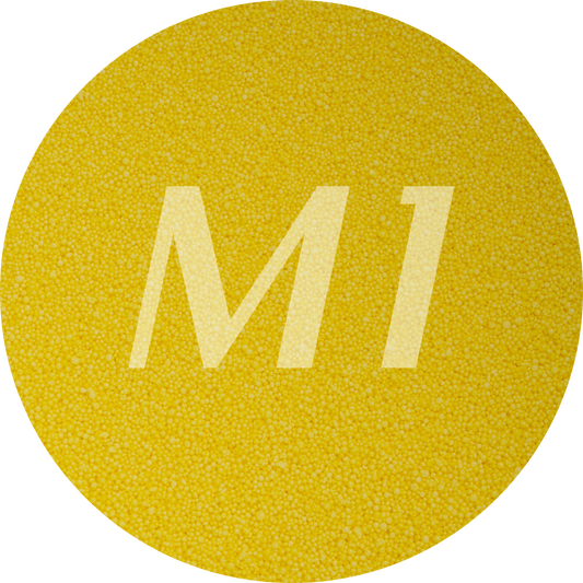 Kleurstaal van geel kaarsenzand met fijne waxparels en subtiel M1-logo op de achtergrond.