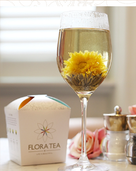 Bloeiende theebloem in hittebestendig Flora Tea wijnglas naast Flora Tea verpakking