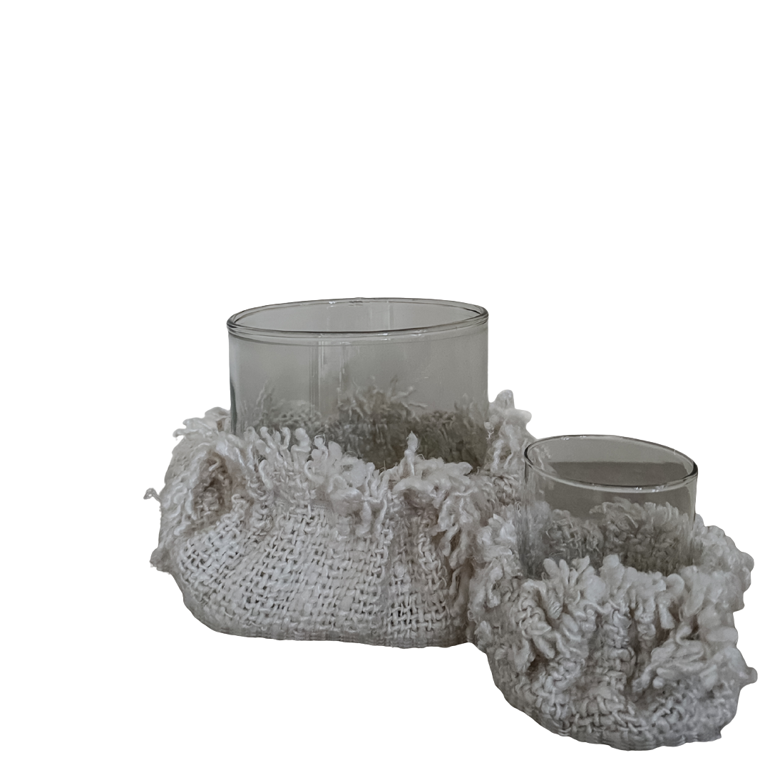 Set van twee glazen kaarsenhouders met decoratieve beige stoffen hoezen in grof geweven en pluizige structuur, op transparante achtergrond.