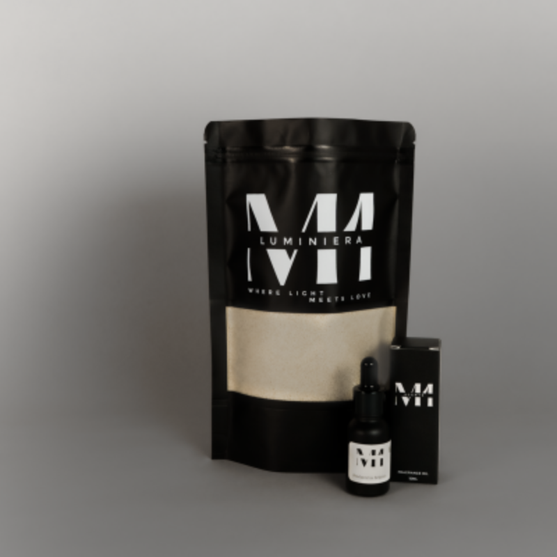 Zwarte verpakking M1 Luminièra kaarsenzand met witte inhoud, vergezeld door een flesje M1 geurolie en bijpassend doosje, op een grijze achtergrond.