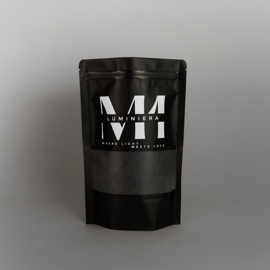 Zwarte staande verpakking van M1 Luminièra kaarsenzand met wit logo en de tekst 'Where Light Meets Love' op een grijze achtergrond.