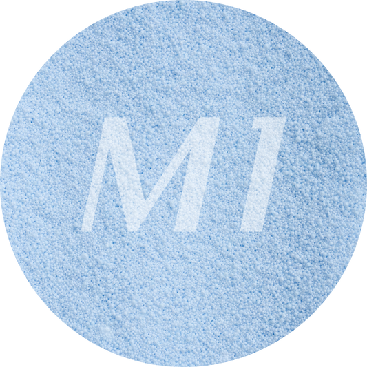 Kleurstaal van licht blauw kaarsenzand met fijne waxparels en subtiel M1-logo op de achtergrond.