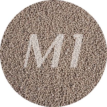 Kleurstaal van bruin kaarsenzand met fijne waxparels en subtiel M1-logo op de achtergrond.