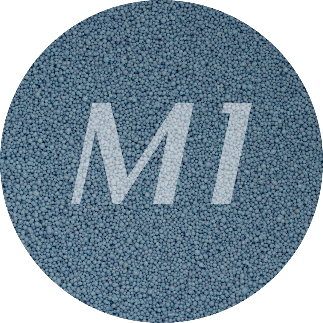 Kleurstaal van blauw kaarsenzand met fijne waxparels en subtiel M1-logo op de achtergrond.