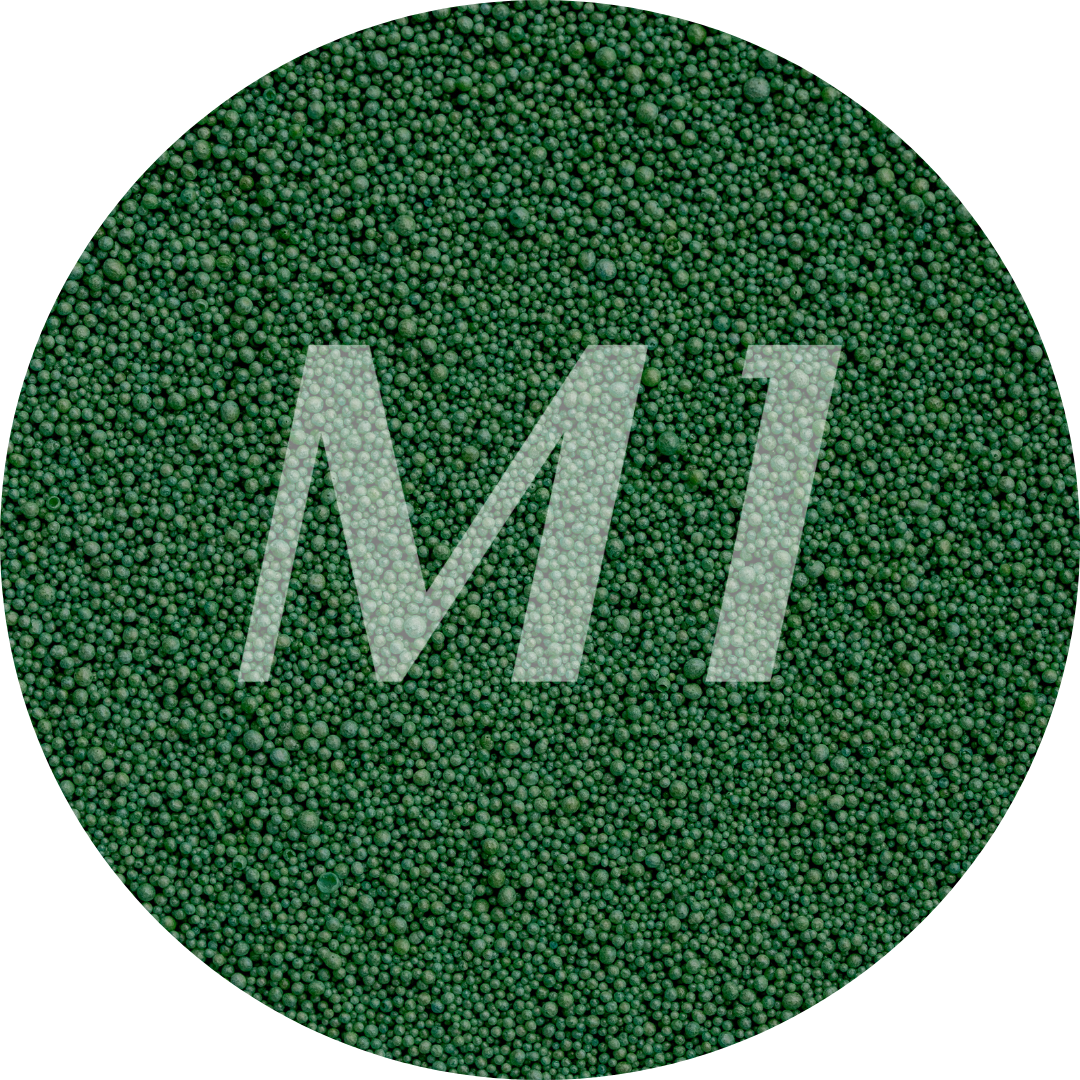 Kleurstaal van donker groen kaarsenzand met fijne waxparels en subtiel M1-logo op de achtergrond.