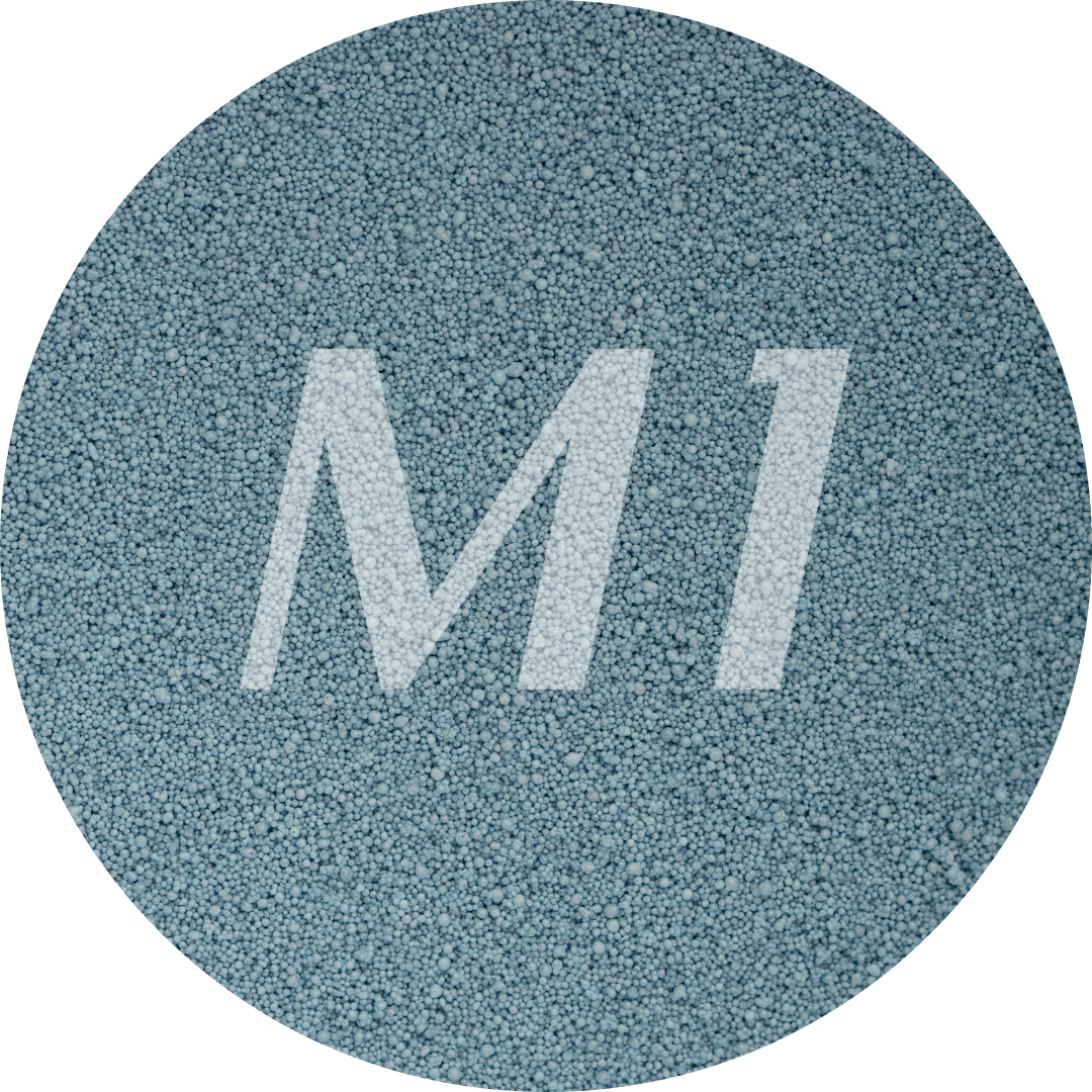 Kleurstaal van grijzig blauw kaarsenzand met fijne waxparels en subtiel M1-logo op de achtergrond.
