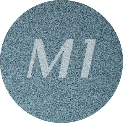 Kleurstaal van grijzig blauw kaarsenzand met fijne waxparels en subtiel M1-logo op de achtergrond.