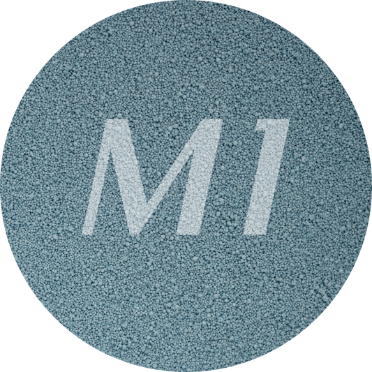 Kleurstaal van grijzig blauw kaarsenzand met fijne waxparels en subtiel M1-logo op de achtergrond.