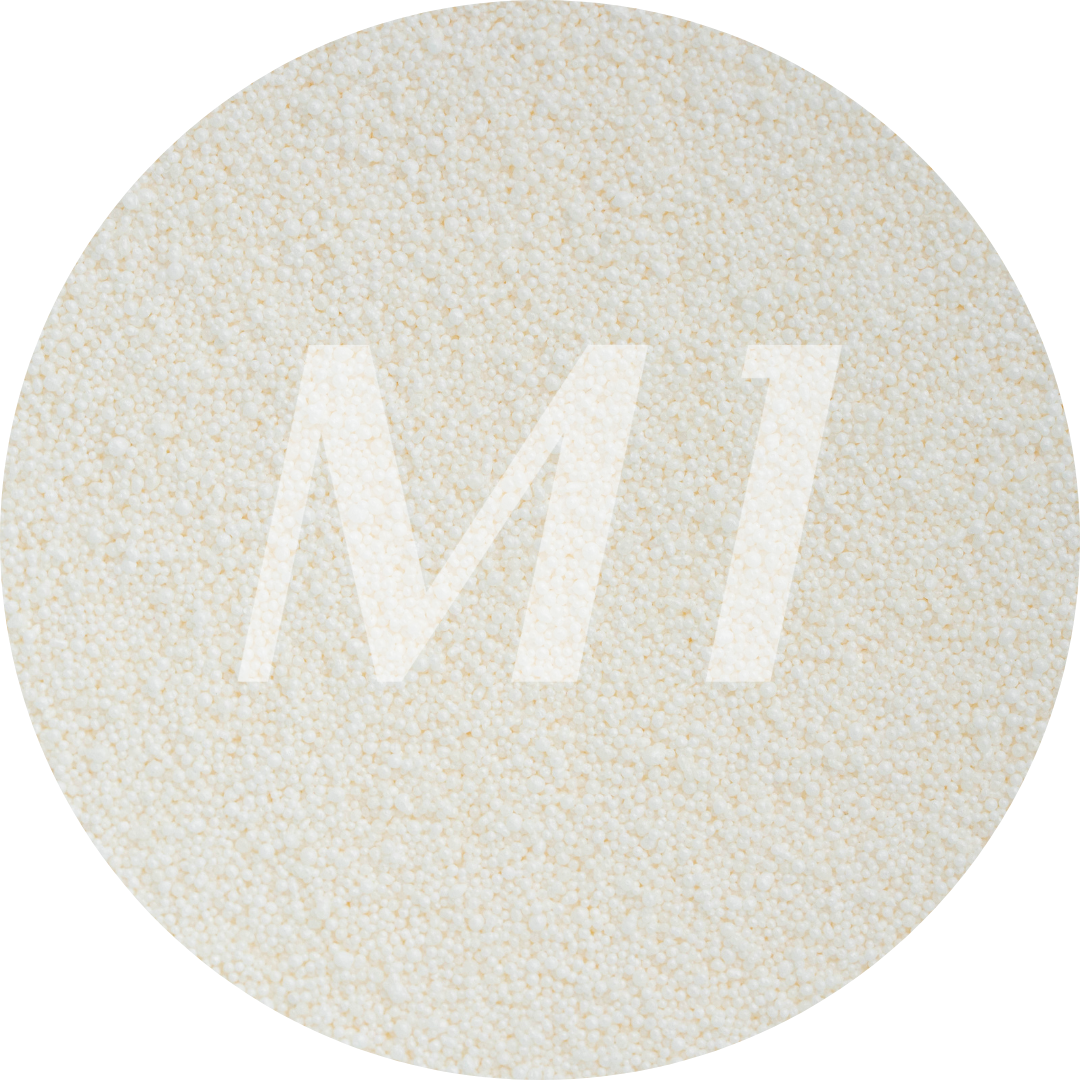 Kleurstaal van gebroken wit kaarsenzand met fijne waxparels en subtiel M1-logo op de achtergrond.