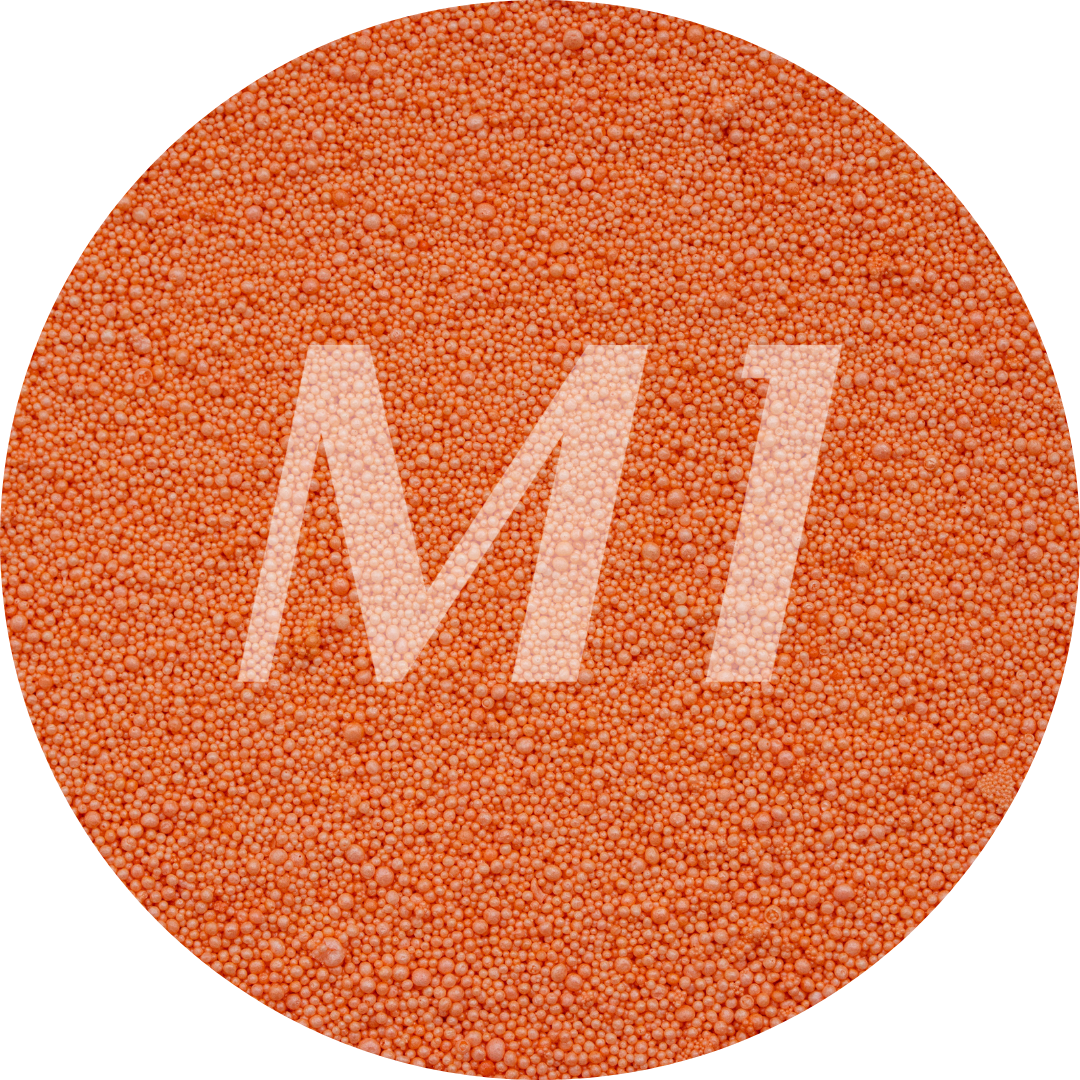 Kleurstaal van oranje kaarsenzand met fijne waxparels en subtiel M1-logo op de achtergrond.