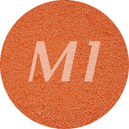 Kleurstaal van oranje kaarsenzand met fijne waxparels en subtiel M1-logo op de achtergrond.