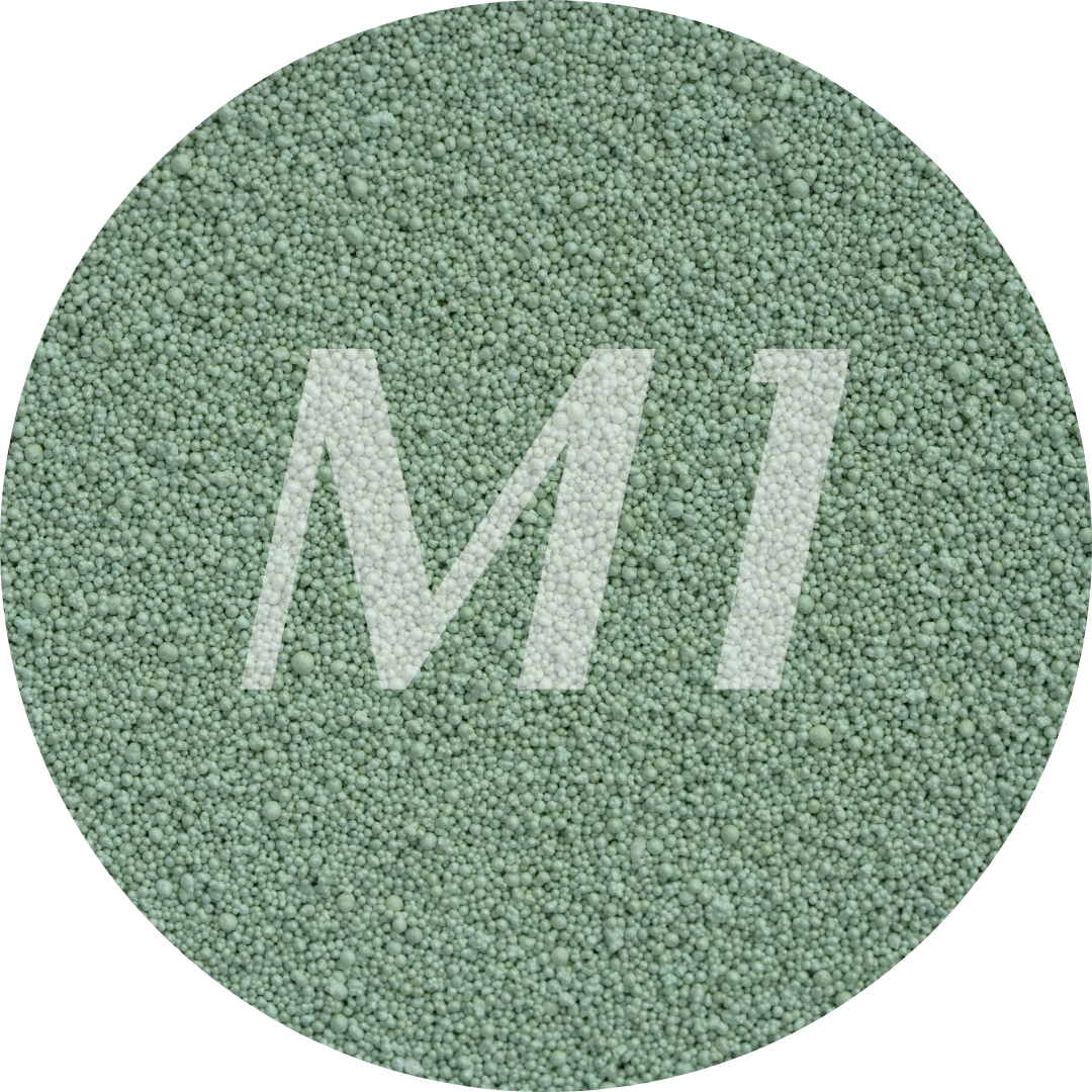 Kleurstaal van groen kaarsenzand met fijne waxparels en subtiel M1-logo op de achtergrond.