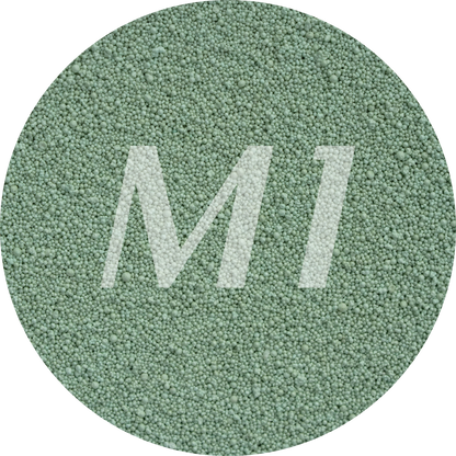 Kleurstaal van groen kaarsenzand met fijne waxparels en subtiel M1-logo op de achtergrond.