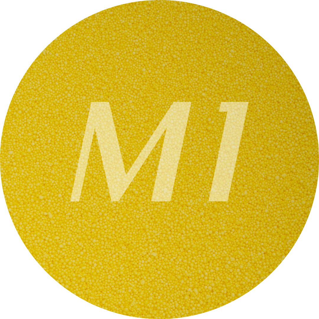 Kleurstaal van geel kaarsenzand met fijne waxparels en subtiel M1-logo op de achtergrond.