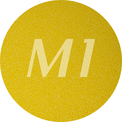Kleurstaal van geel kaarsenzand met fijne waxparels en subtiel M1-logo op de achtergrond.