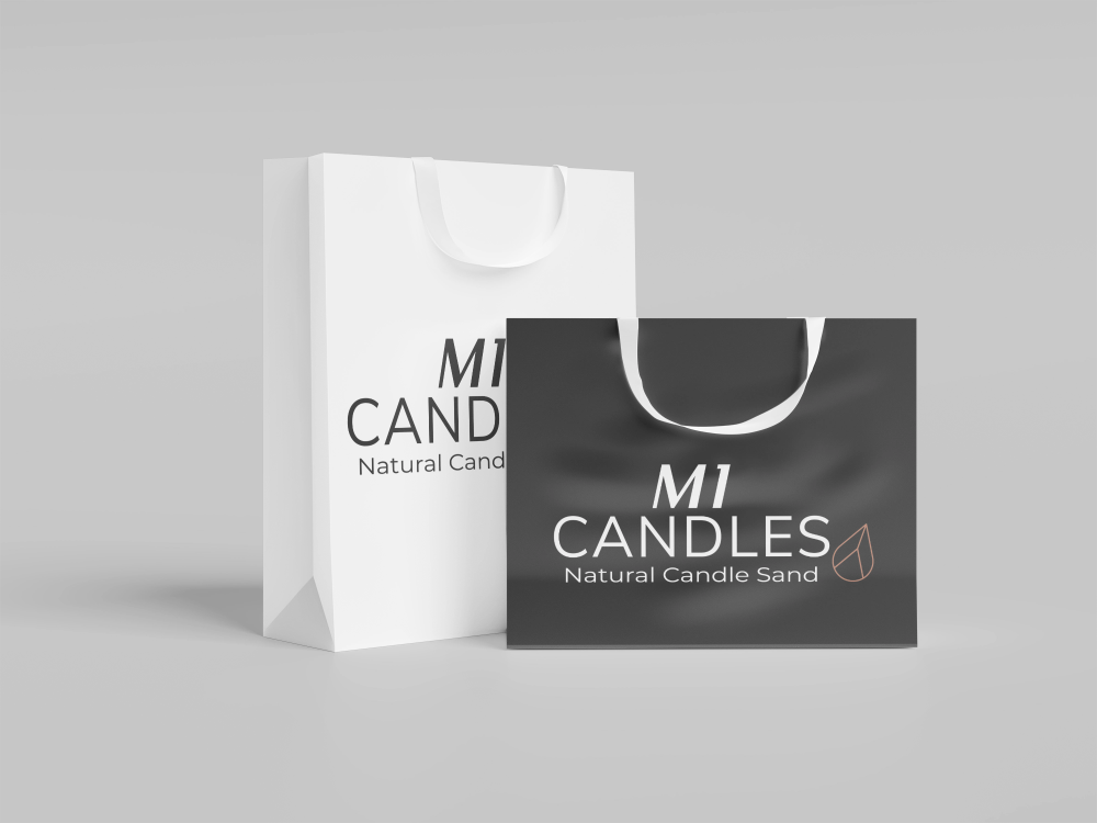 Twee shoppingtassen met M1 Candles-logo en de tekst 'Natural Candle Sand', één in het wit en één in het zwart, op een grijze achtergrond.