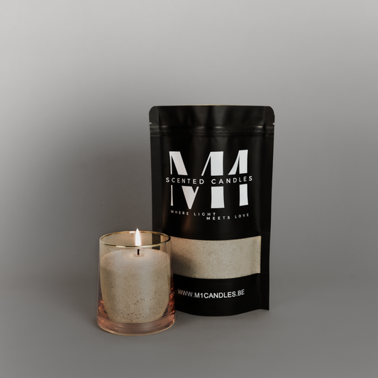 Zwarte verpakking van M1 Scented Candles kaarsenzand met zandkleurige inhoud, naast een brandende kaars in een glas met goudkleurige rand, op een grijze achtergrond.