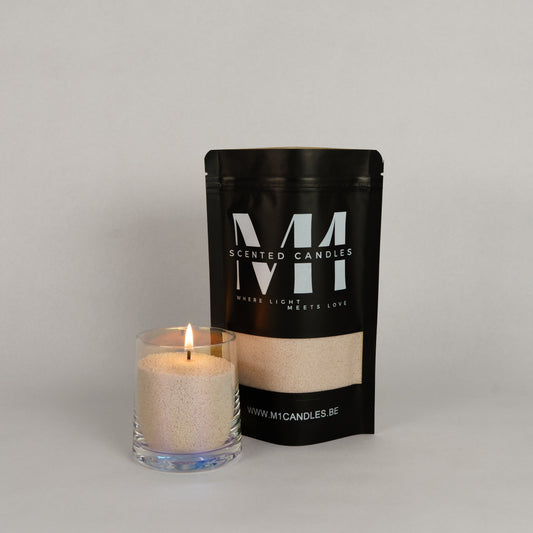 Verpakking van M1 Scented Candles kaarsenzand in een zwarte zak met logo, naast een glazen houder gevuld met brandend kaarsenzand.