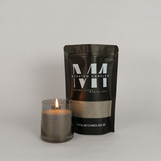 Verpakking van M1 Scented Candles kaarsenzand in een zwarte zak met logo, naast een glazen houder gevuld met brandend grijs kaarsenzand.