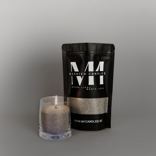 Zwarte verpakking van M1 Scented Candles kaarsenzand met een brandende kaars in een transparante glazen houder ernaast, op een grijze achtergrond.
