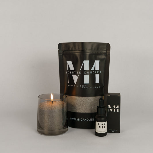 Productset van M1 Candles met een brandende kaars in glas gevuld met kaarsenzand, een zwarte verpakking met M1-logo, en een flesje geurolie met bijhorende doos.