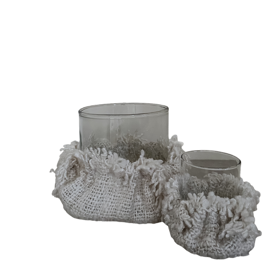 Set van twee glazen kaarsenhouders met decoratieve beige stoffen hoezen in grof geweven en pluizige structuur, op transparante achtergrond.