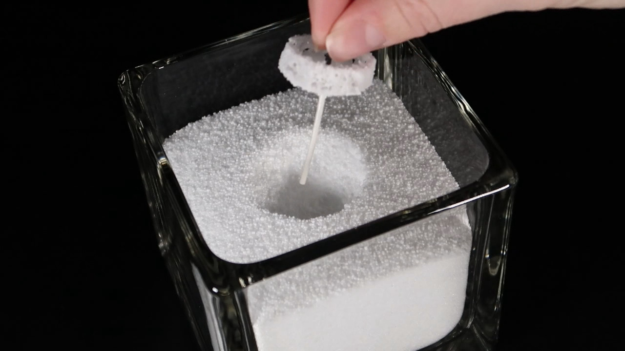 Close-up van een lont die in kaarsenzand wordt geplaatst in een glazen kaarshouder voor het maken van een nieuwe kaars.